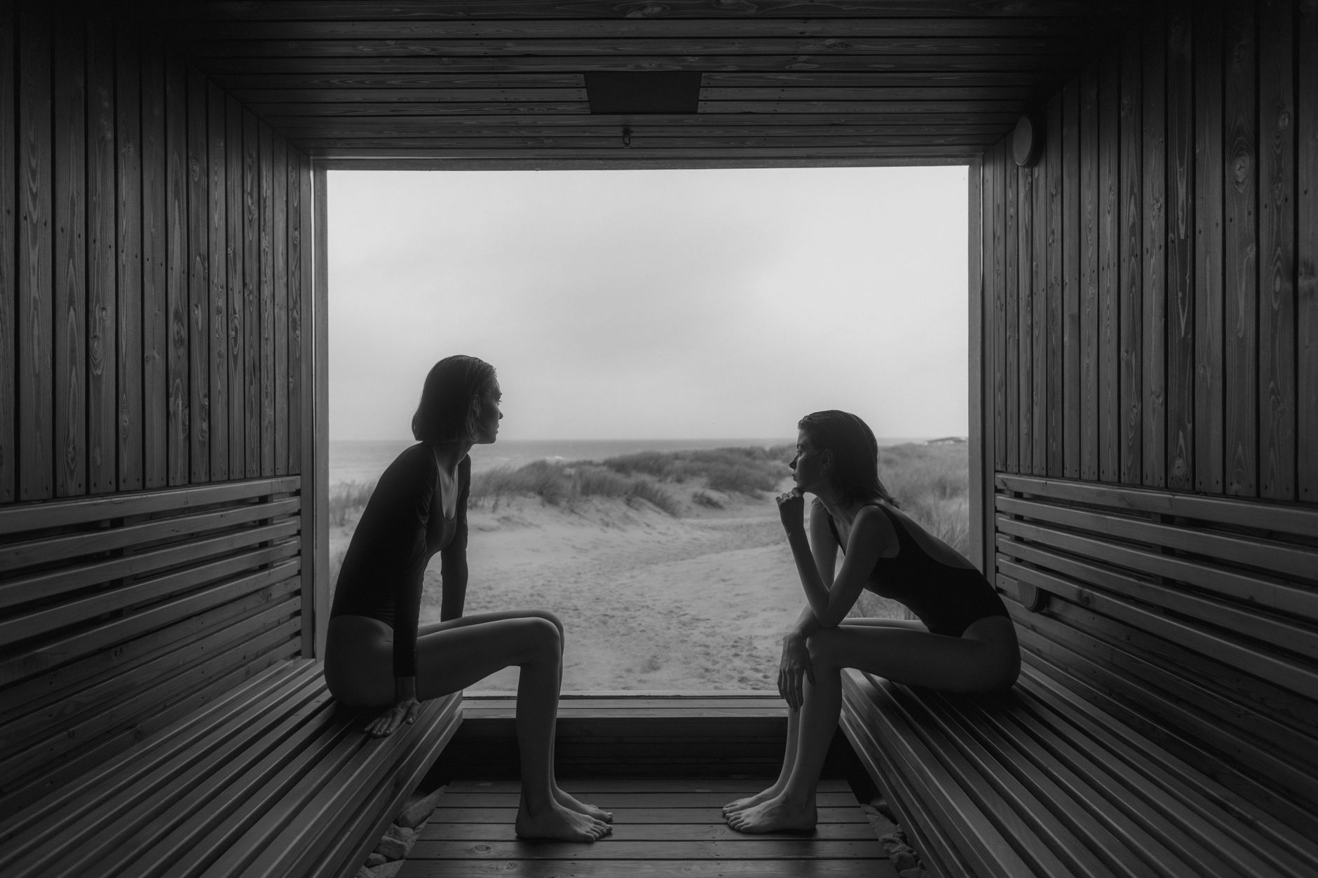grayscale photo of women sitting on wooden bench