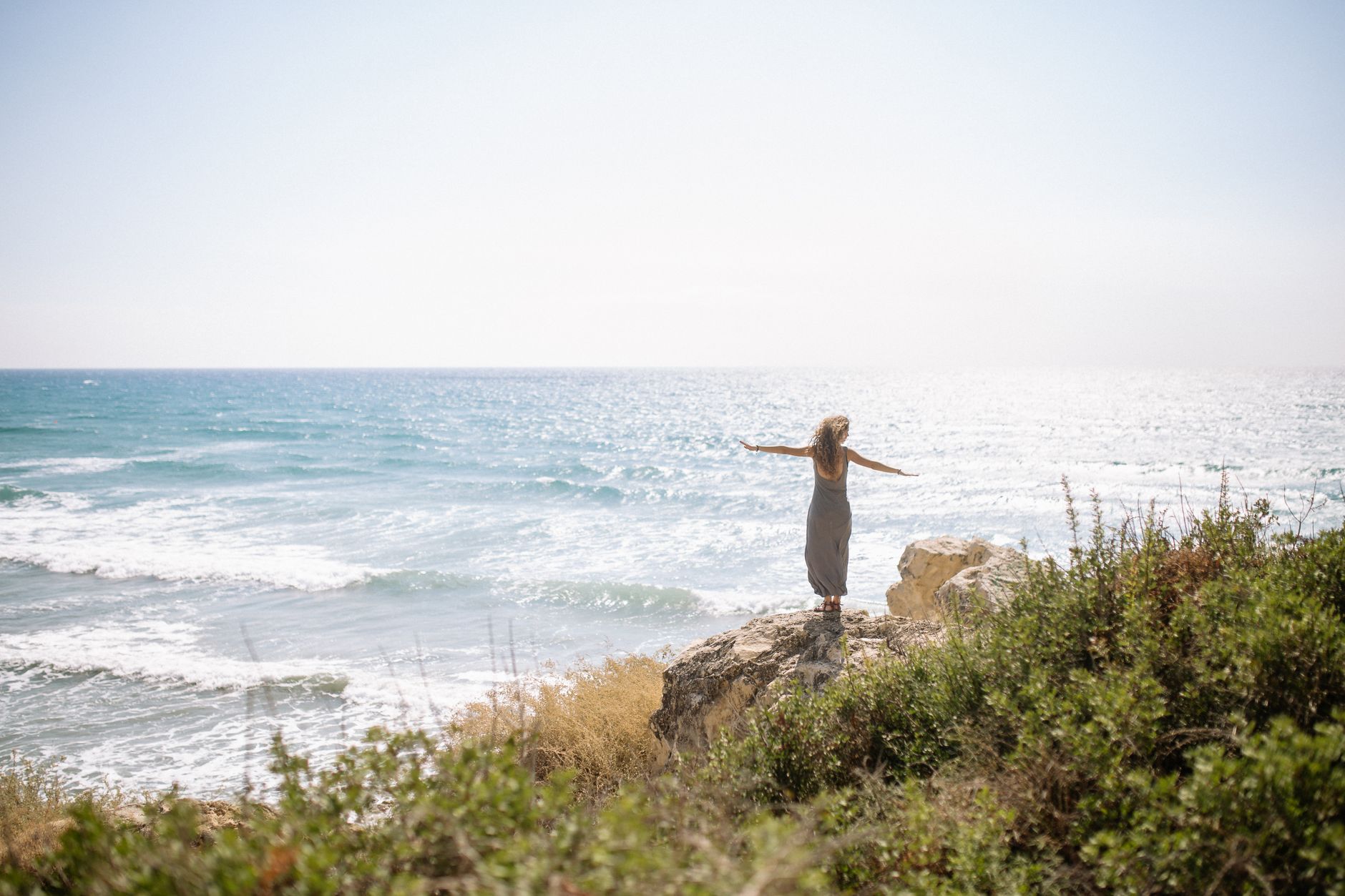 woman in long dress standing on rock near body of water